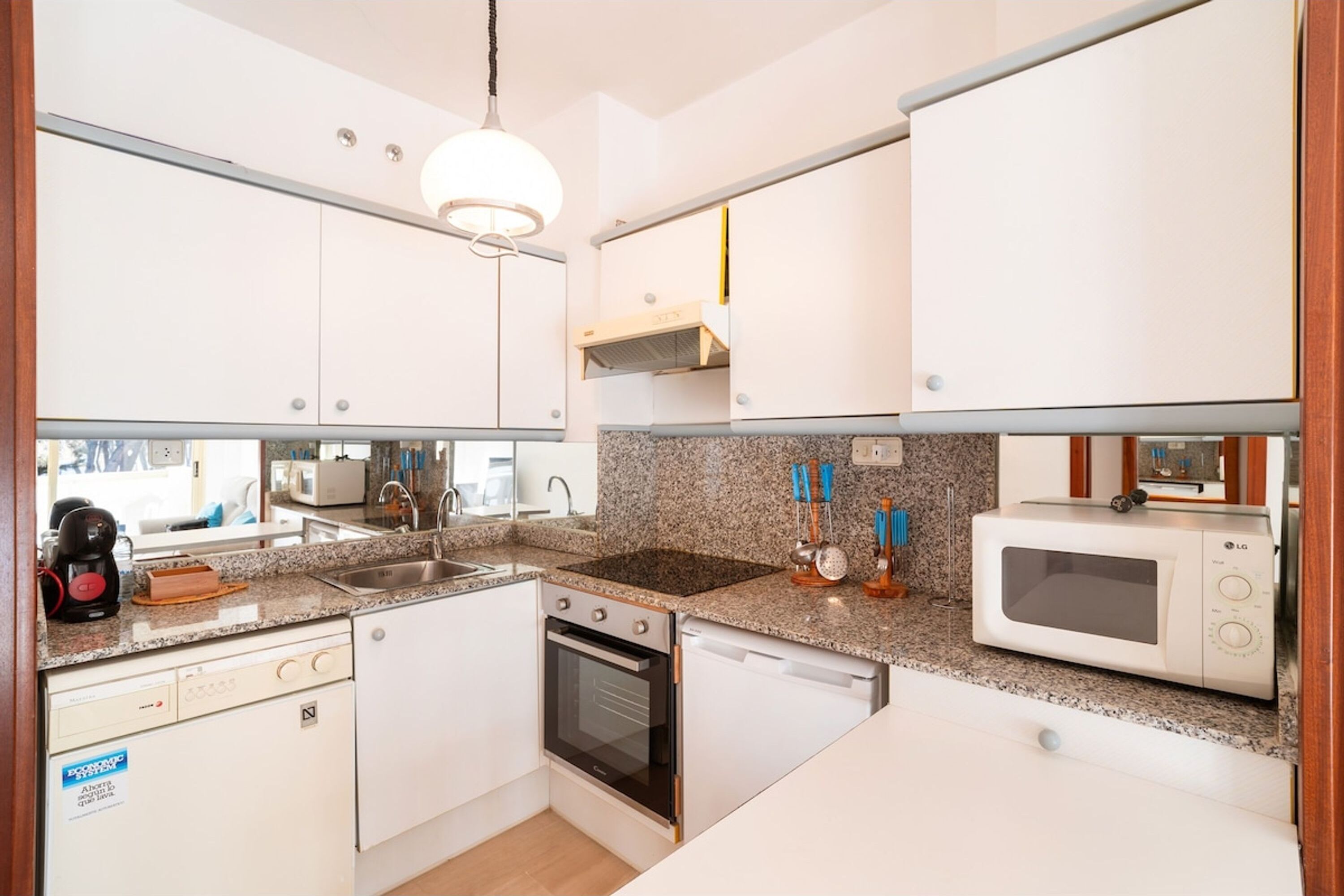 A compact kitchen with white cabinets, a built-in oven, a microwave, and a granite countertop.