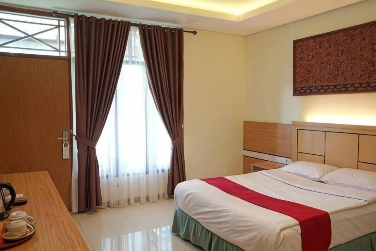 A hotel room with a bed, bedside table, and a window with curtains.