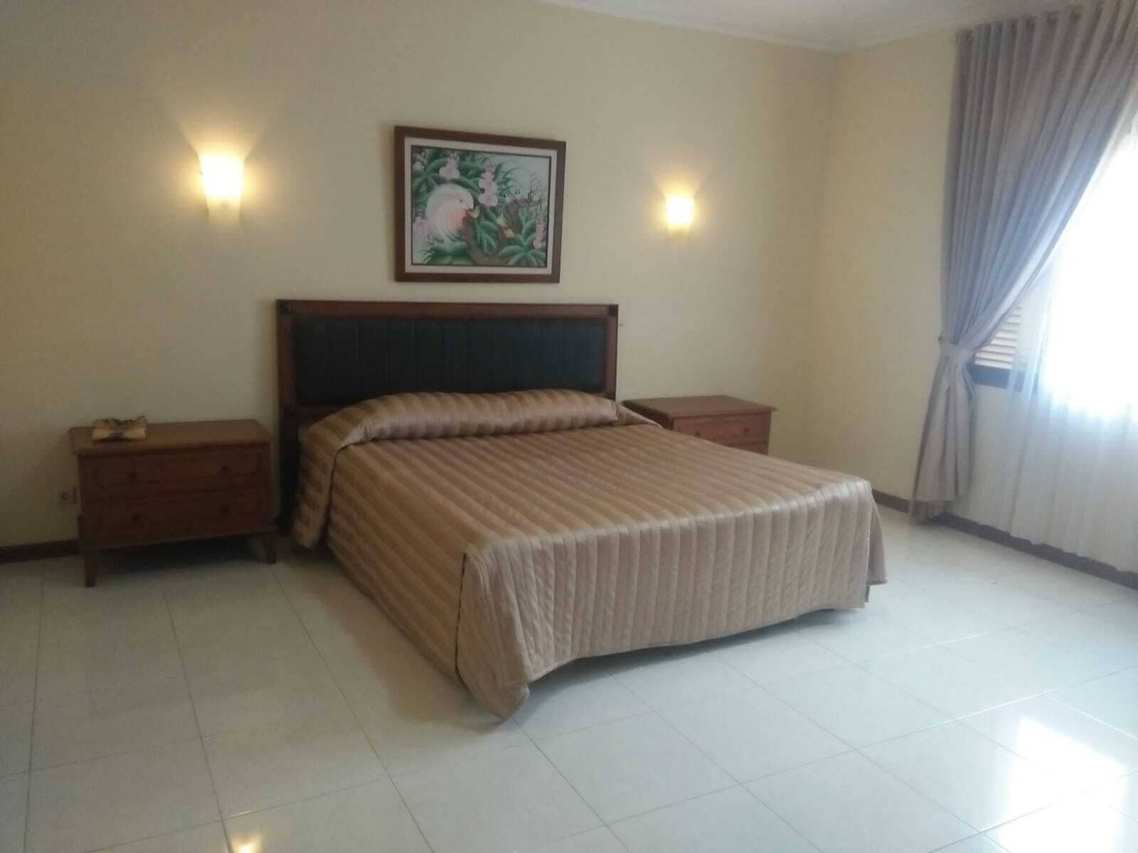 Une chambre à coucher avec un grand lit, deux tables de chevet, une commode, un tableau au mur et une fenêtre avec des rideaux.
