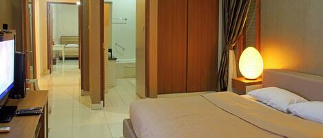 A hotel room with a bed, bedside table, and a television. There is a bathroom visible through an open door.