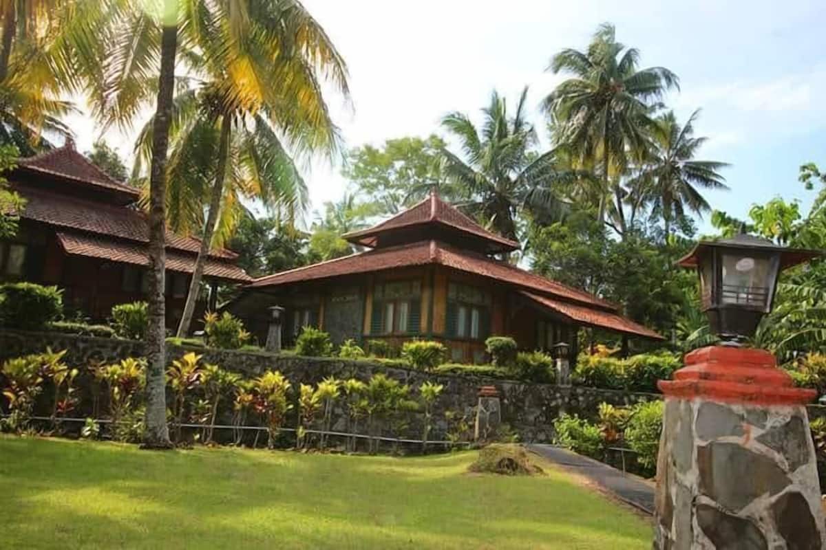 A traditional-style building with a tiled roof, surrounded by lush greenery and palm trees.