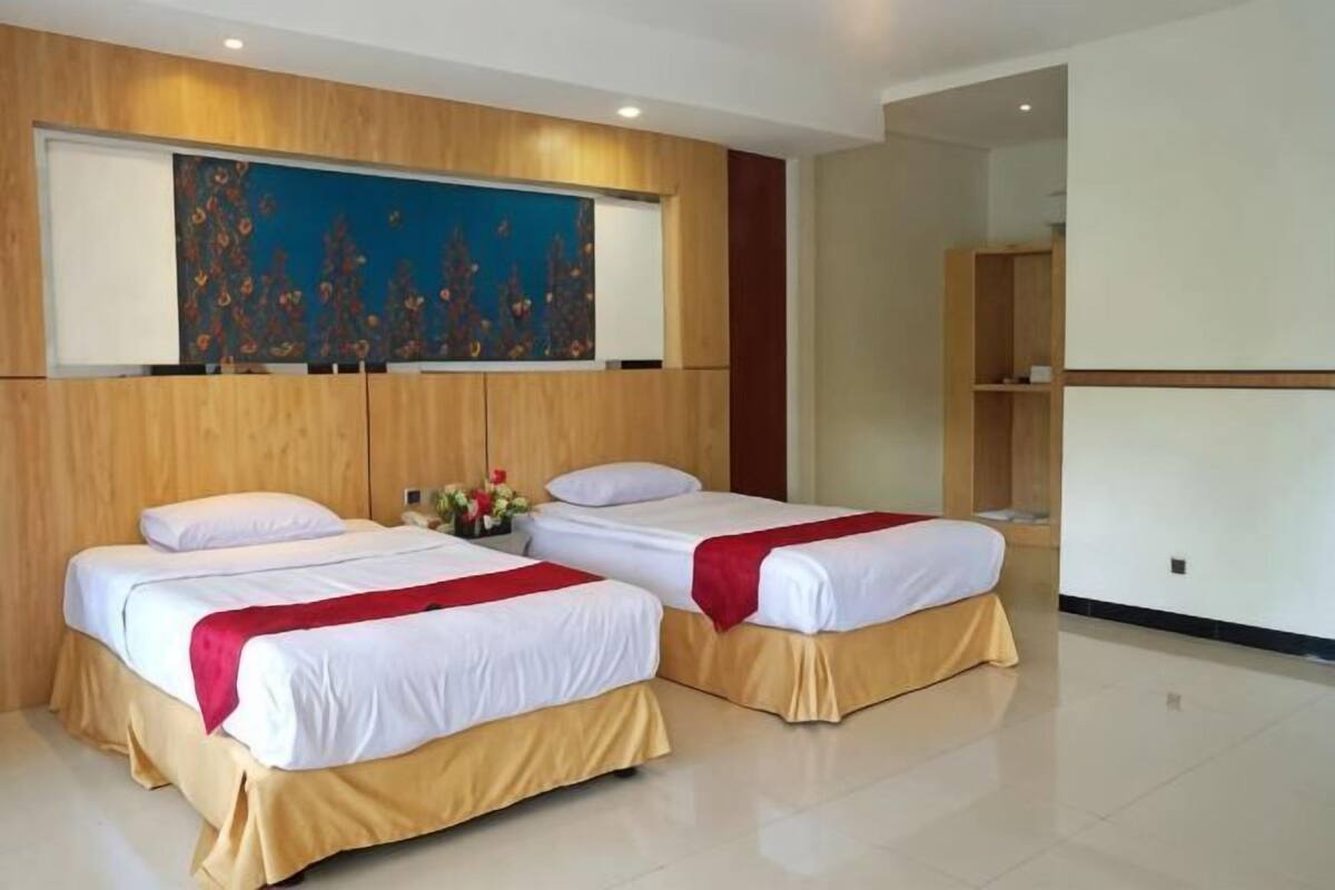A hotel room with two beds, a wooden headboard, a large abstract painting, and a bookshelf.