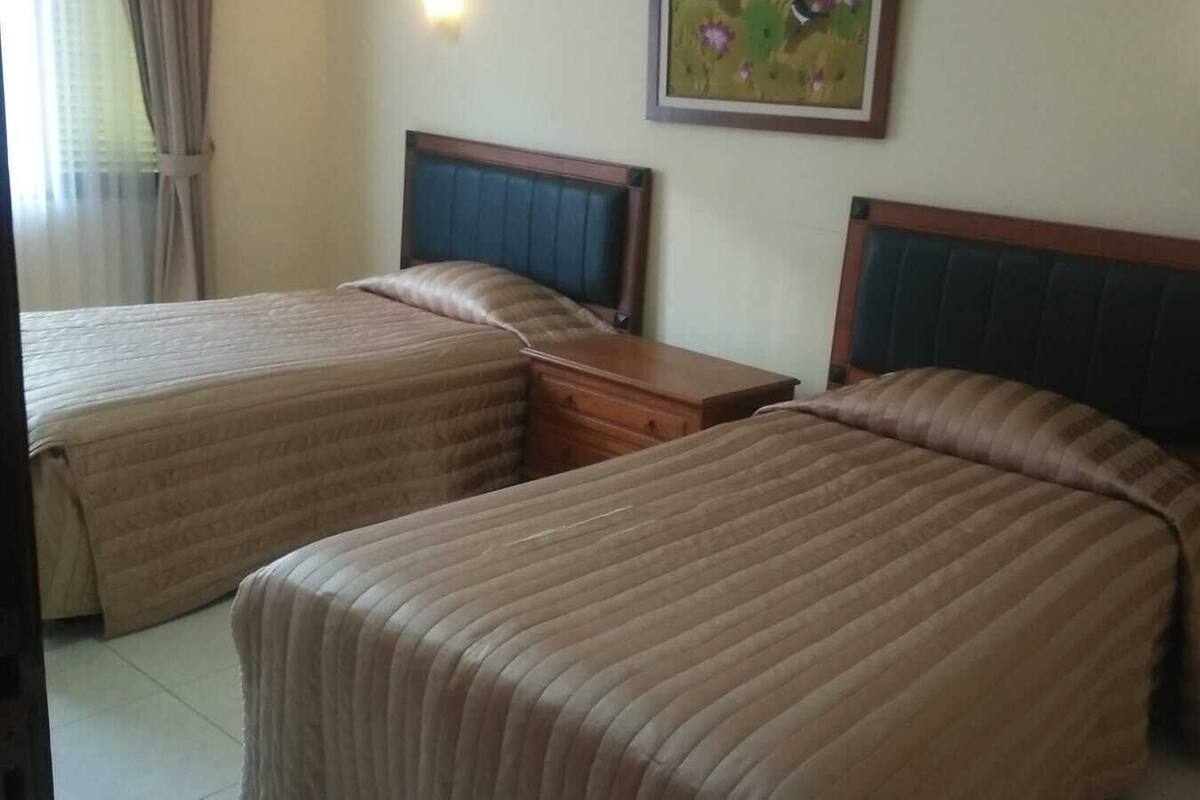 A hotel room with two beds, a wooden nightstand, and a painting on the wall.
