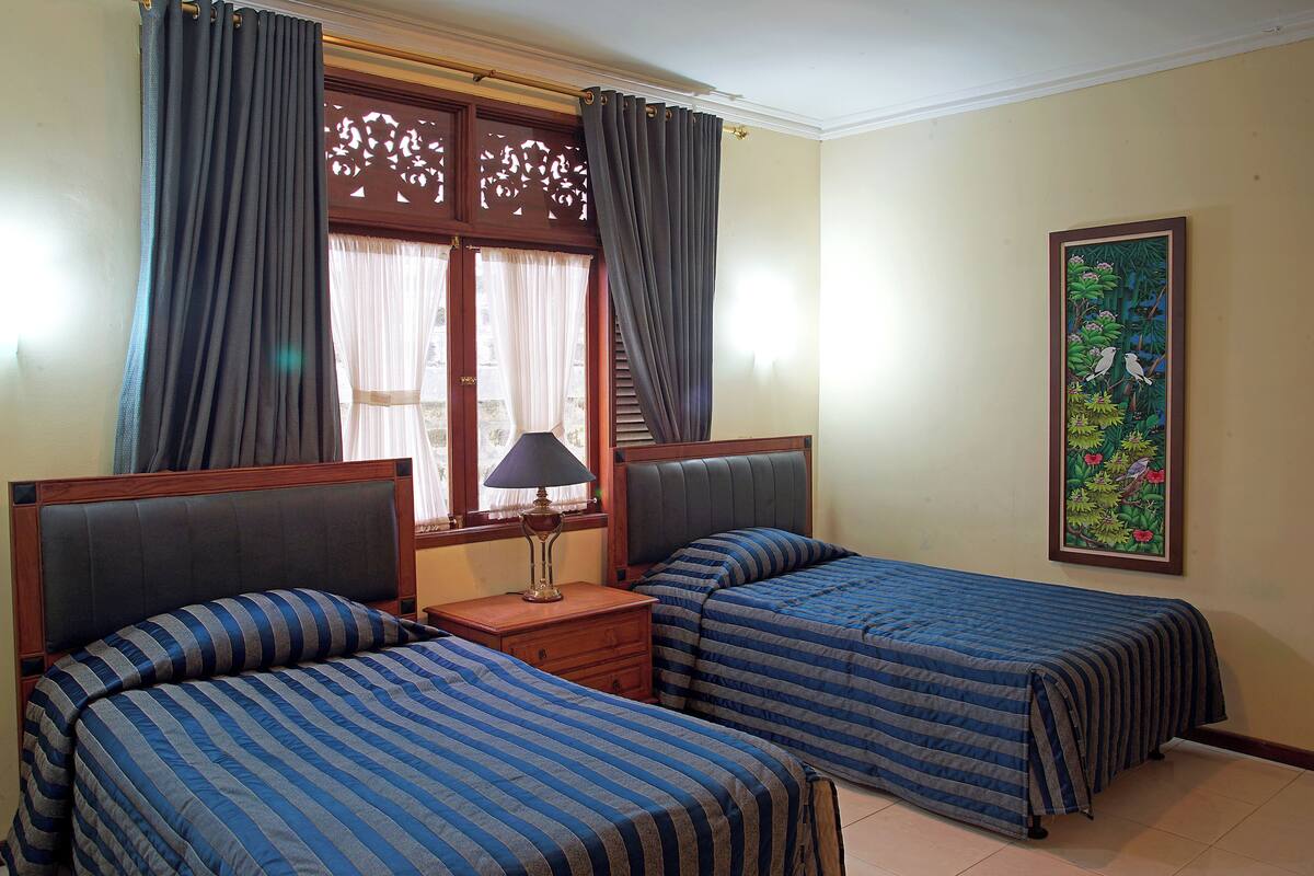 A room with two beds, a nightstand, a lamp, and a window with curtains.