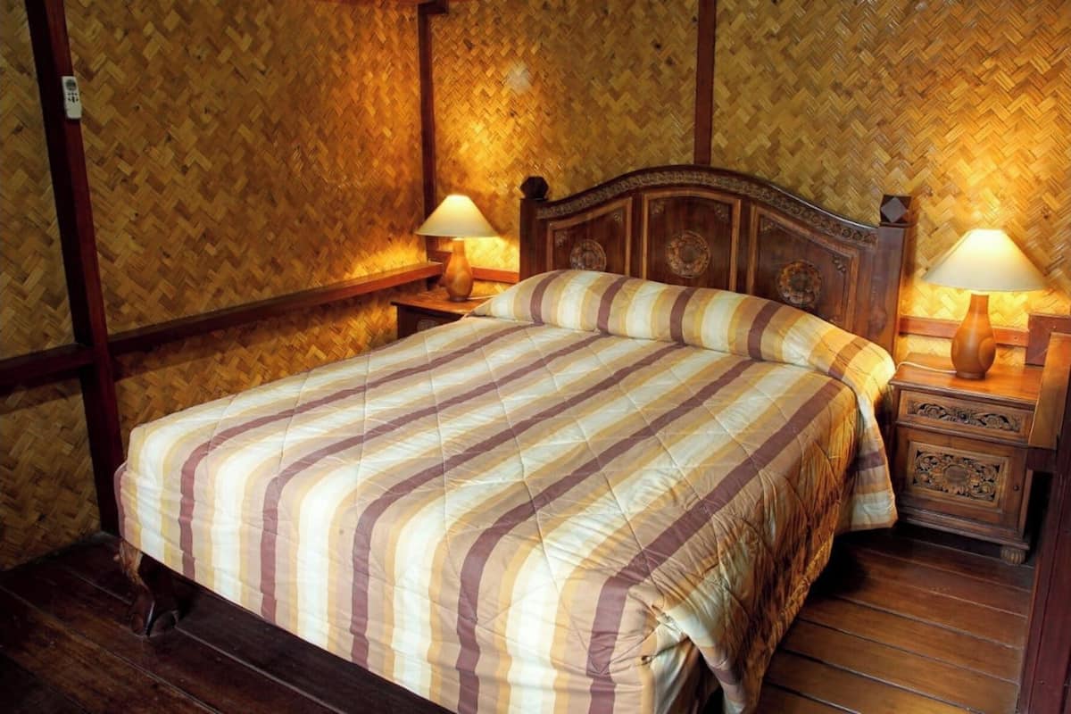 A bed with a striped bedspread, two bedside tables with lamps, and a wooden headboard.