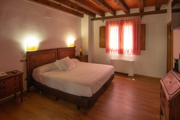 A bedroom with a wooden bed, two bedside lamps, a wooden dresser, and a window with curtains. - Hospedium Hotel Rural Abadia de Yuste (Cuacos de Yuste)