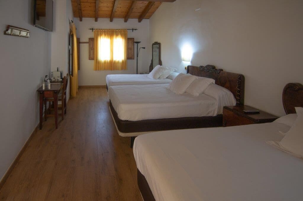 Habitación de hotel con dos camas, suelo de madera, un escritorio con silla y una ventana con cortinas.