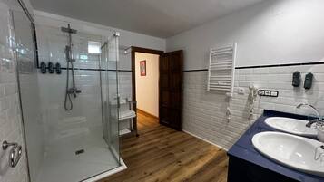 A modern bathroom with a glass shower enclosure, wooden flooring, a white toilet, and two sinks with faucets.