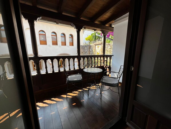 A wooden balcony with a table and chairs, a stone wall, and arched windows. - Hospedium Hotel Rural Abadia de Yuste (Cuacos de Yuste)
