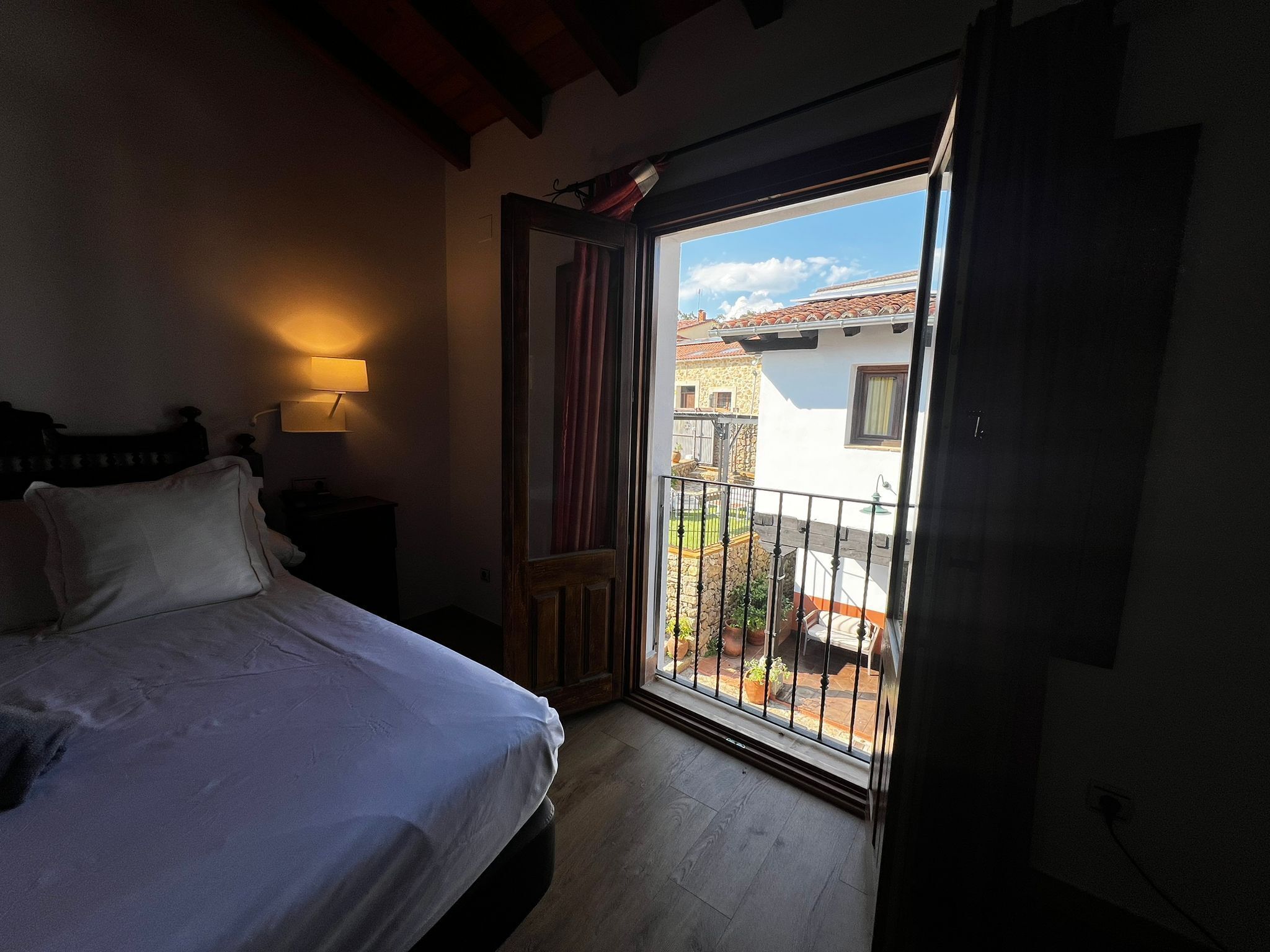 A bedroom with a bed, a nightstand, a lamp, and a balcony with a view of a building.