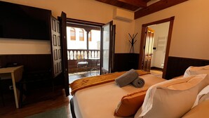 A hotel room with a bed, a desk, and a chair. There is a balcony with a railing and a view of buildings outside. - Hospedium Hotel Rural Abadia de Yuste (Cuacos de Yuste)