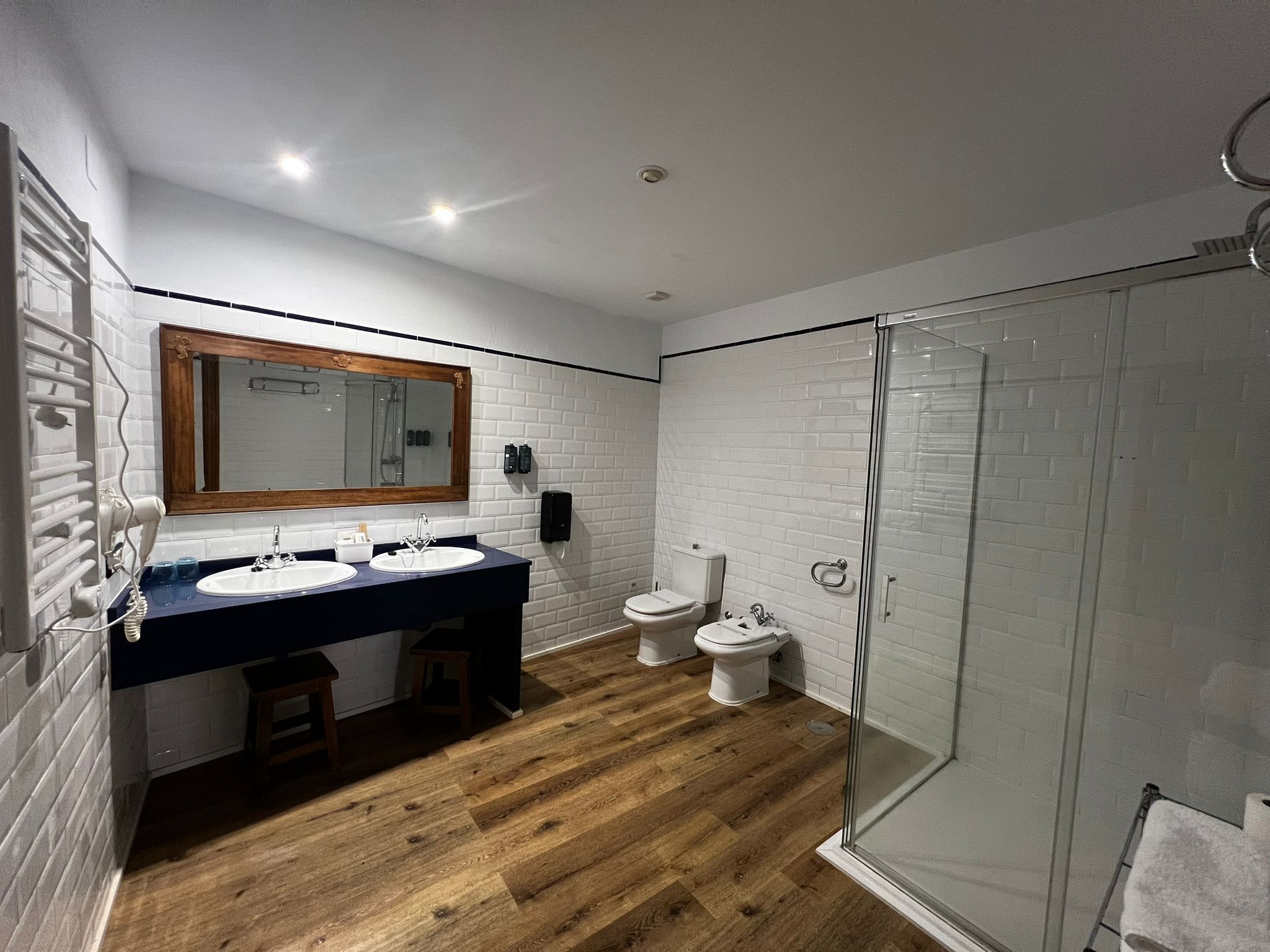 Een moderne badkamer met twee wastafels, een grote spiegel, een toilet en een douche met glazen wanden.