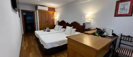 A hotel room with two beds, a wooden desk, a chair, a TV, a lamp, and a framed picture on the wall.
