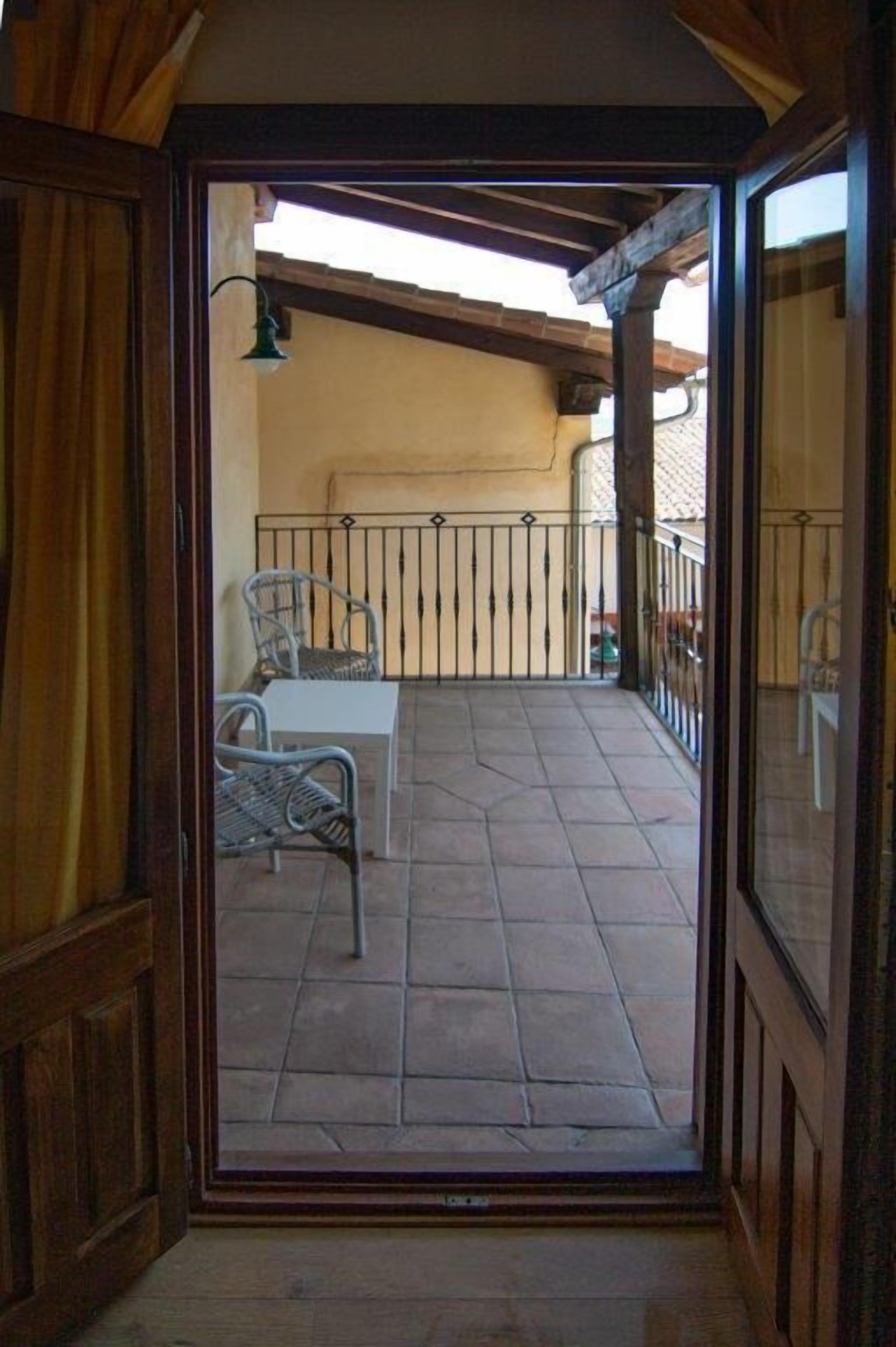 An open door leading to a balcony with a tiled floor, two wicker chairs, a small table, and a metal railing.