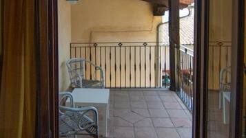 An open door leading to a balcony with a tiled floor, two wicker chairs, a small table, and a metal railing.