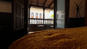 A room with a large, fluffy yellow rug, a wooden door leading to an outdoor balcony with a view of a building with arched windows, and a chair on the balcony. - Hospedium Hotel Rural Abadia de Yuste (Cuacos de Yuste)