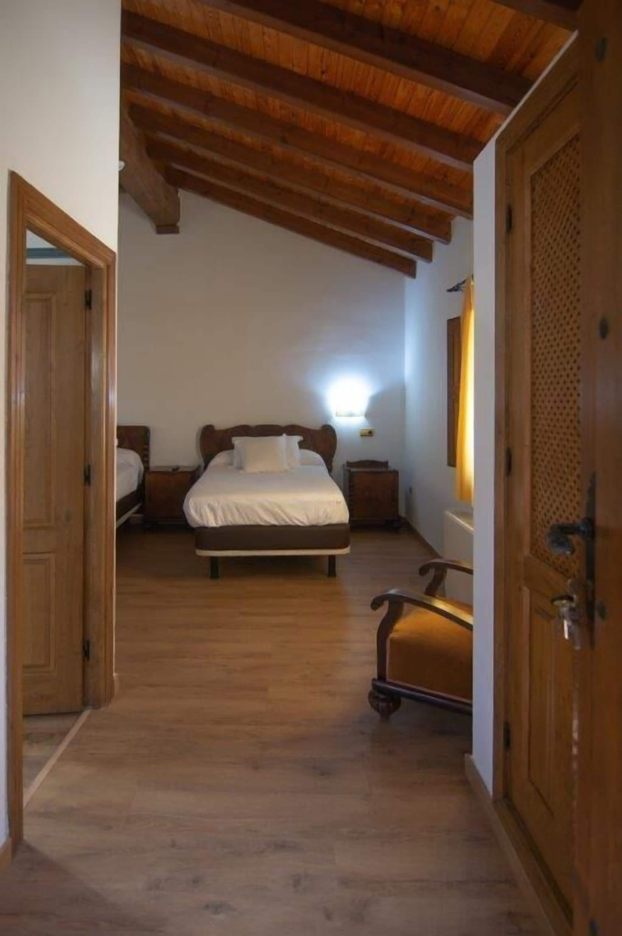 A bedroom with a wooden ceiling, a bed, a nightstand, and a chair.