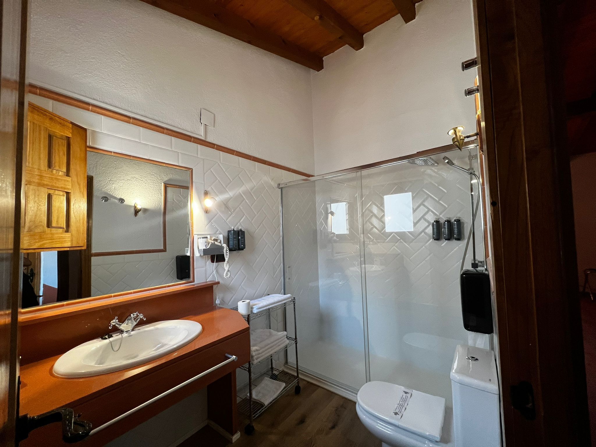 Un baño con tocador de madera, un espejo grande, cabina de ducha de vidrio y un inodoro.