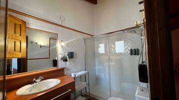Un baño con tocador de madera, un espejo grande, cabina de ducha de vidrio y un inodoro.