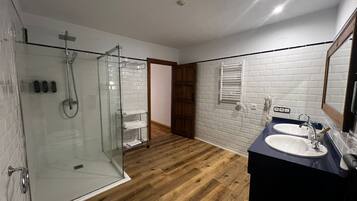 Un baño moderno con ducha envuelta en vidrio, suelo de madera, pared de azulejos blancos y un tocador oscuro con espejo.