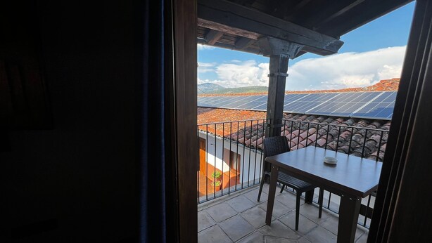 A balcony with a table and chairs, overlooking solar panels and a mountainous landscape.
