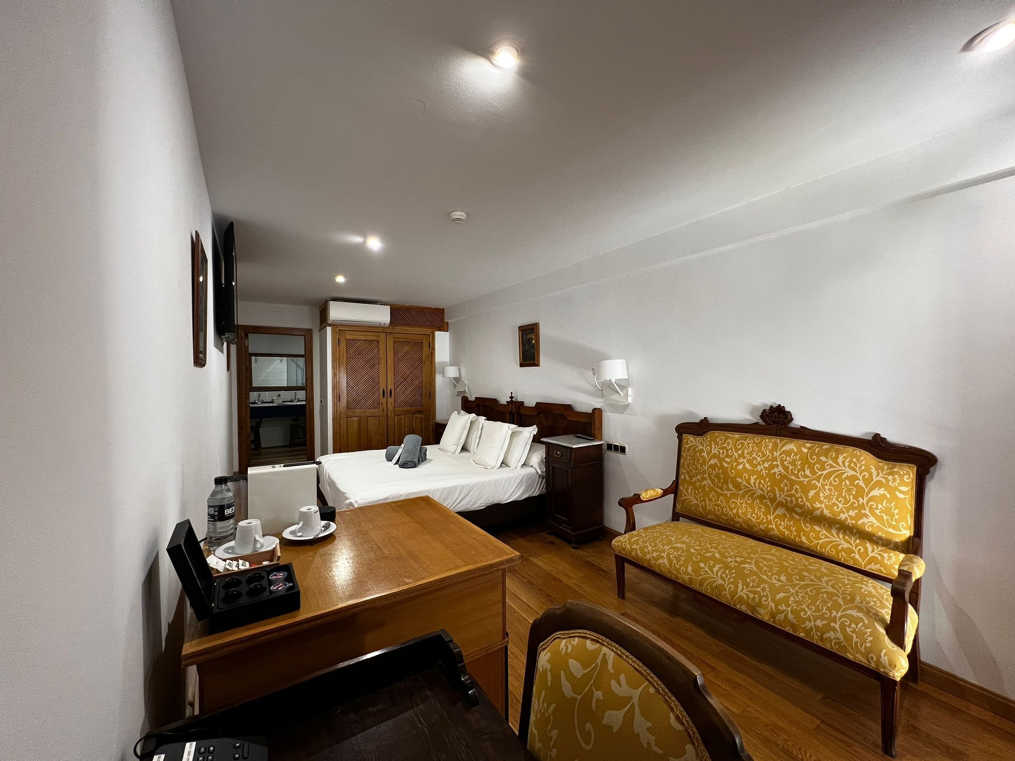 A hotel room with a bed, a desk with a computer, a chair, a sofa, and a wardrobe.