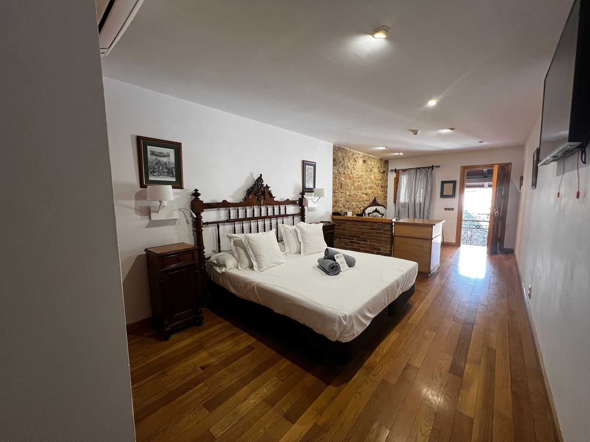 Un dormitorio con cama de madera, cómoda, pared decorativa de piedra y vistas al exterior.