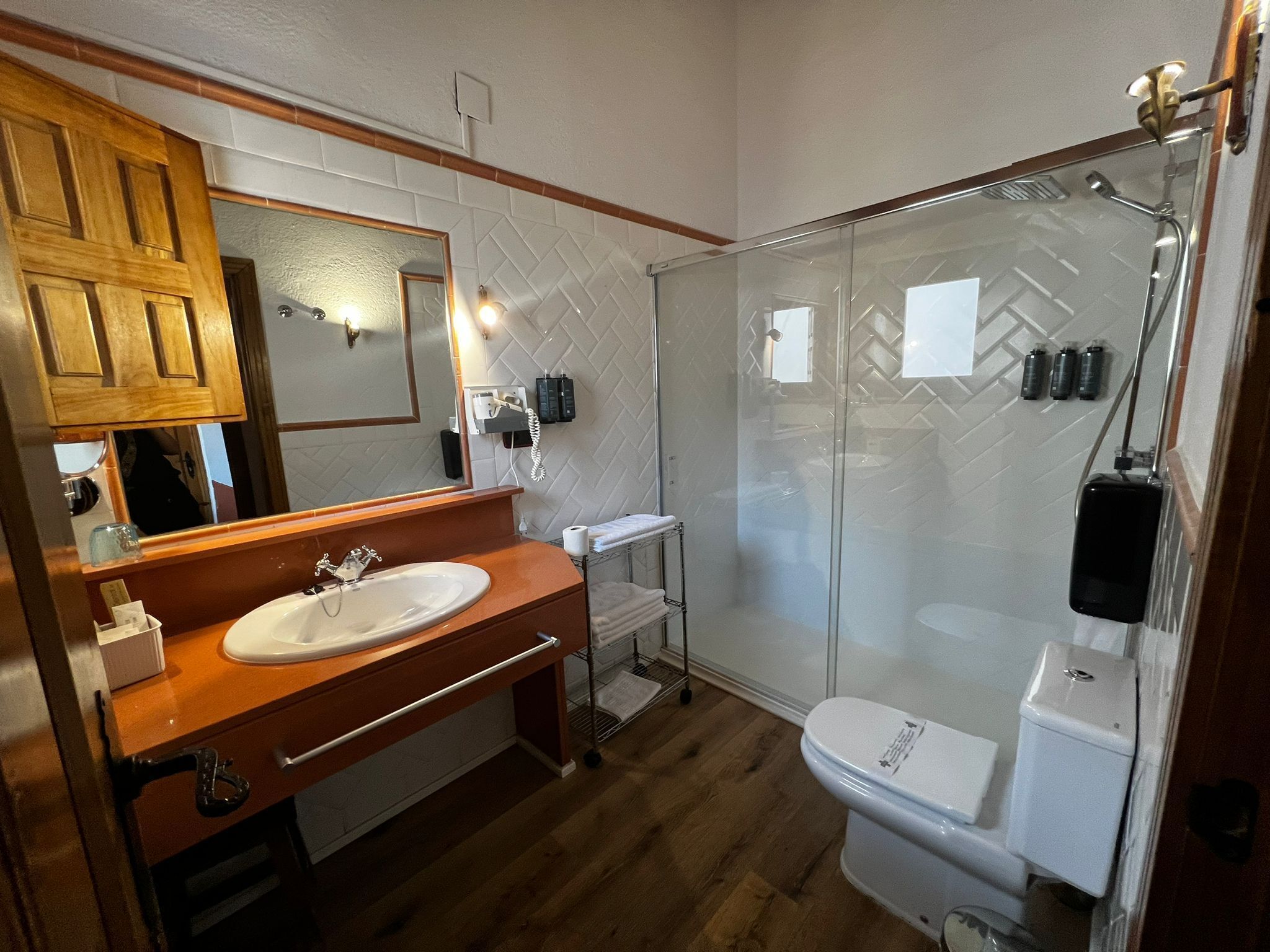 Ein Badezimmer mit einem Holzkosmetikschrank, einem großen Spiegel, einer Duschkabine aus Glas und einer Toilette.