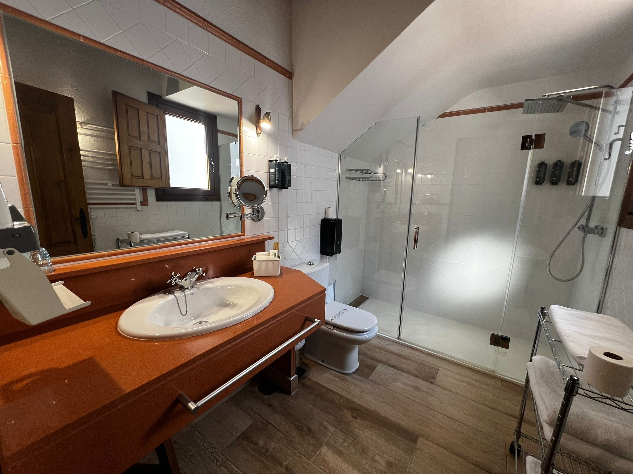 Un baño moderno con tocador de madera, un espejo grande, cabina de ducha de vidrio y un inodoro.