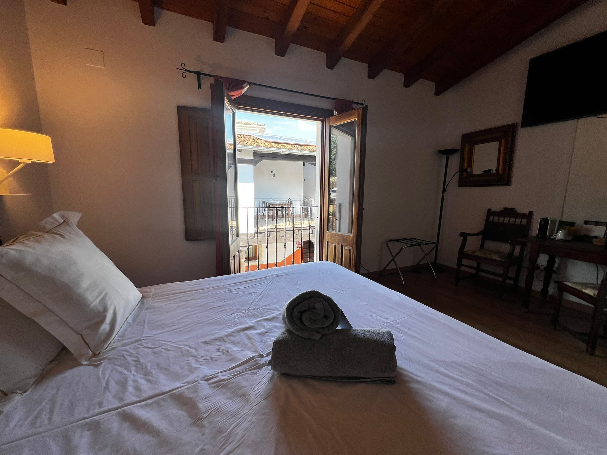Ein Schlafzimmer mit Bett, Schreibtisch, Stuhl und einem Balkon mit Geländer.