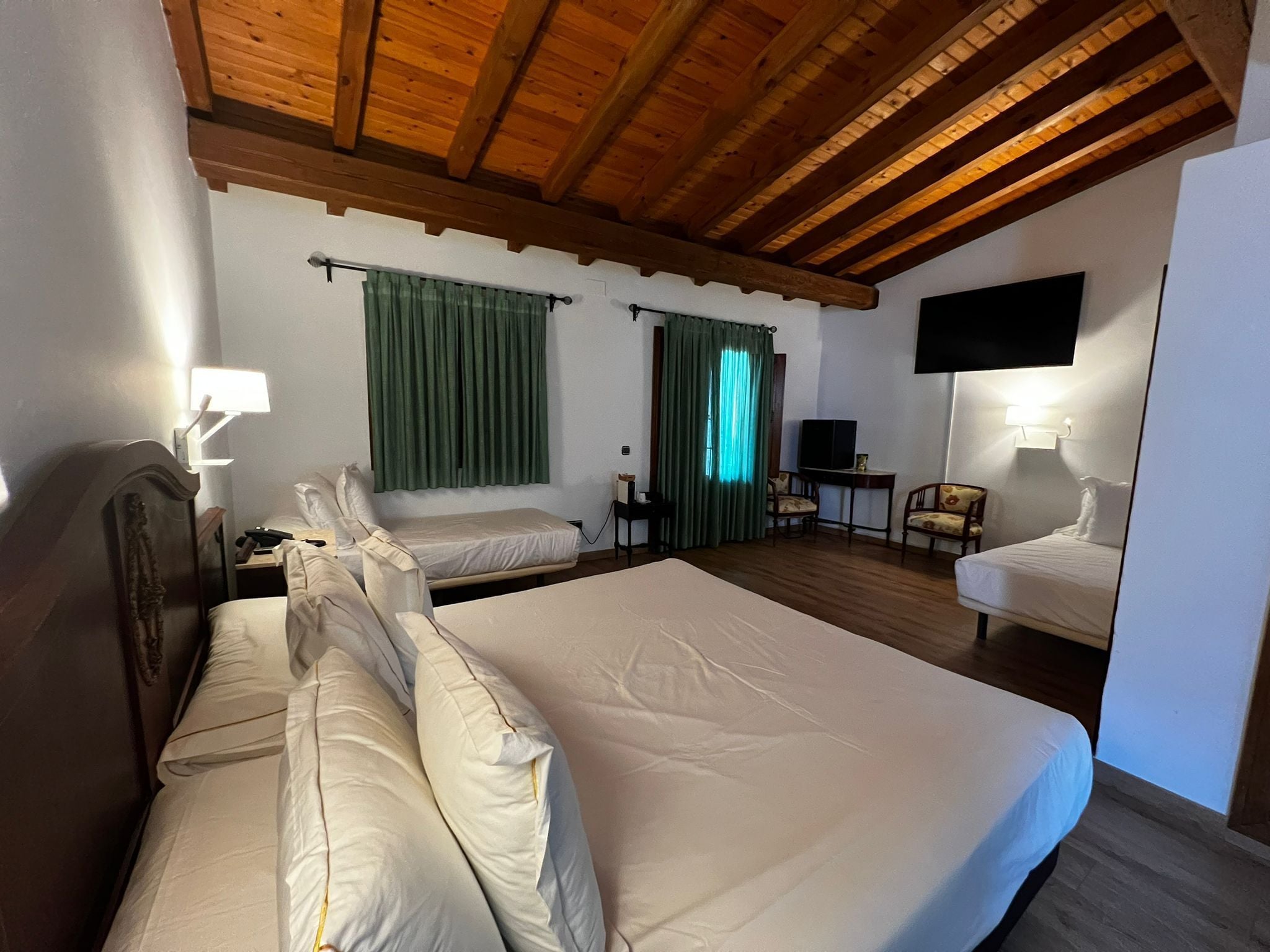Una habitación de hotel con una cama grande, televisión, escritorio con silla y ventana con cortinas.