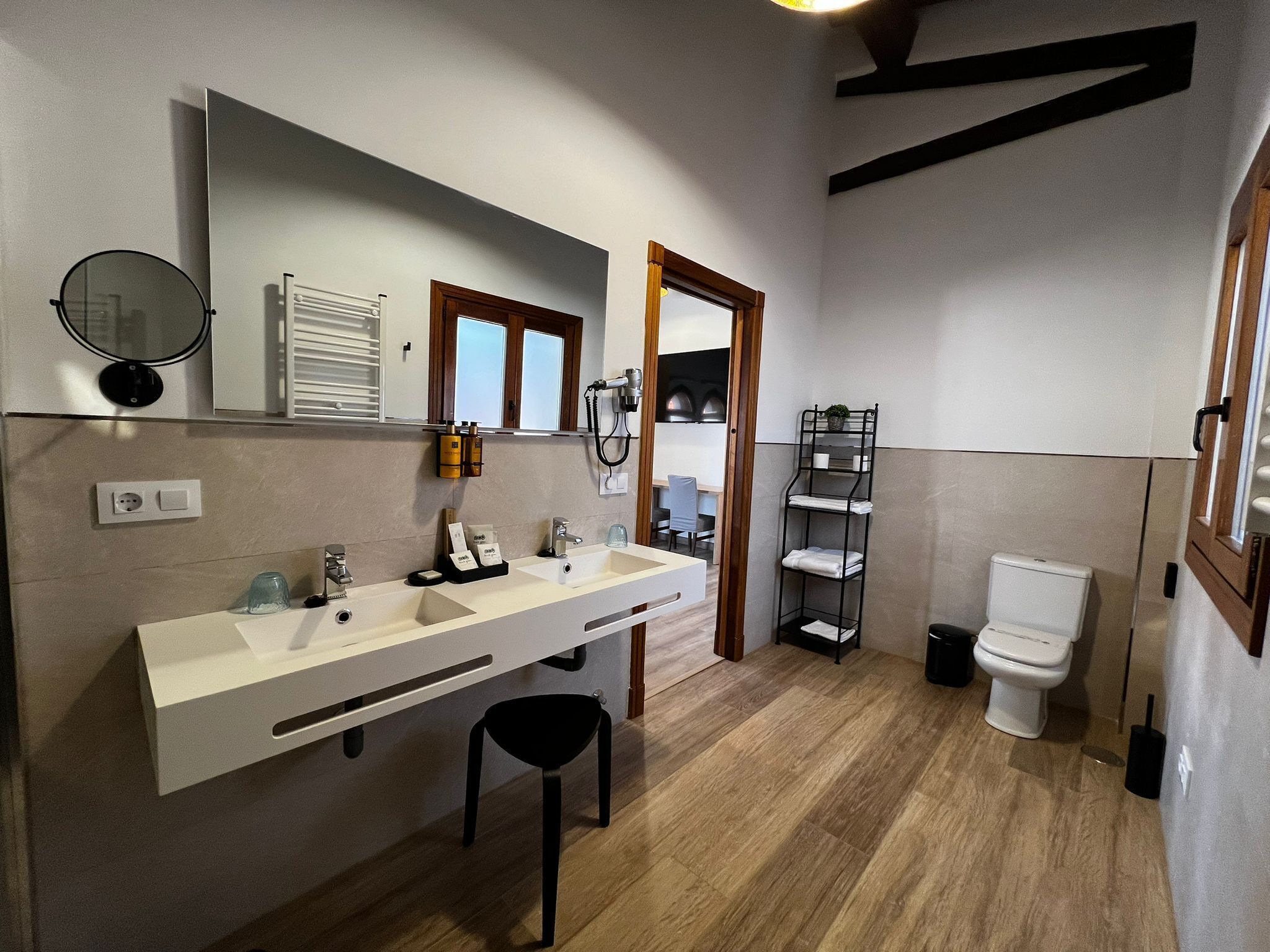 A modern bathroom with a large mirror, two sinks, a toilet, and a shower area.