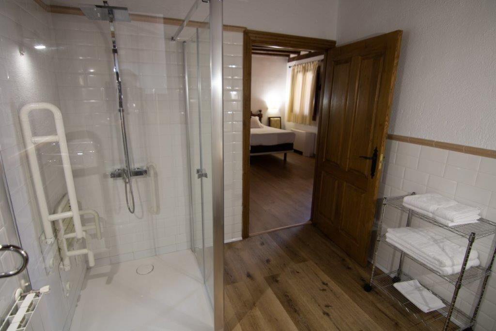 Un baño con ducha de vidrio, un perchero blanco y una puerta de madera que da a un dormitorio.