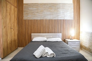 A bedroom with a bed, two pillows, a nightstand, and a wooden wardrobe. - Kritos Apartments With Two Bedrooms (Argaka)