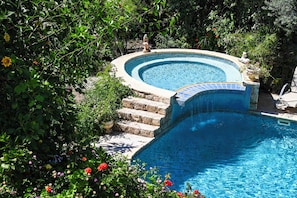 Ein Schwimmbecken mit Steinbord, umgeben von üppiger Bepflanzung und Blumen.