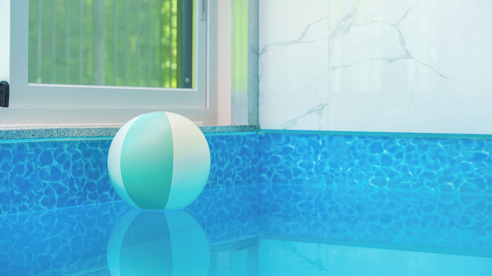 A clear view of a swimming pool with a single beach ball on the edge.