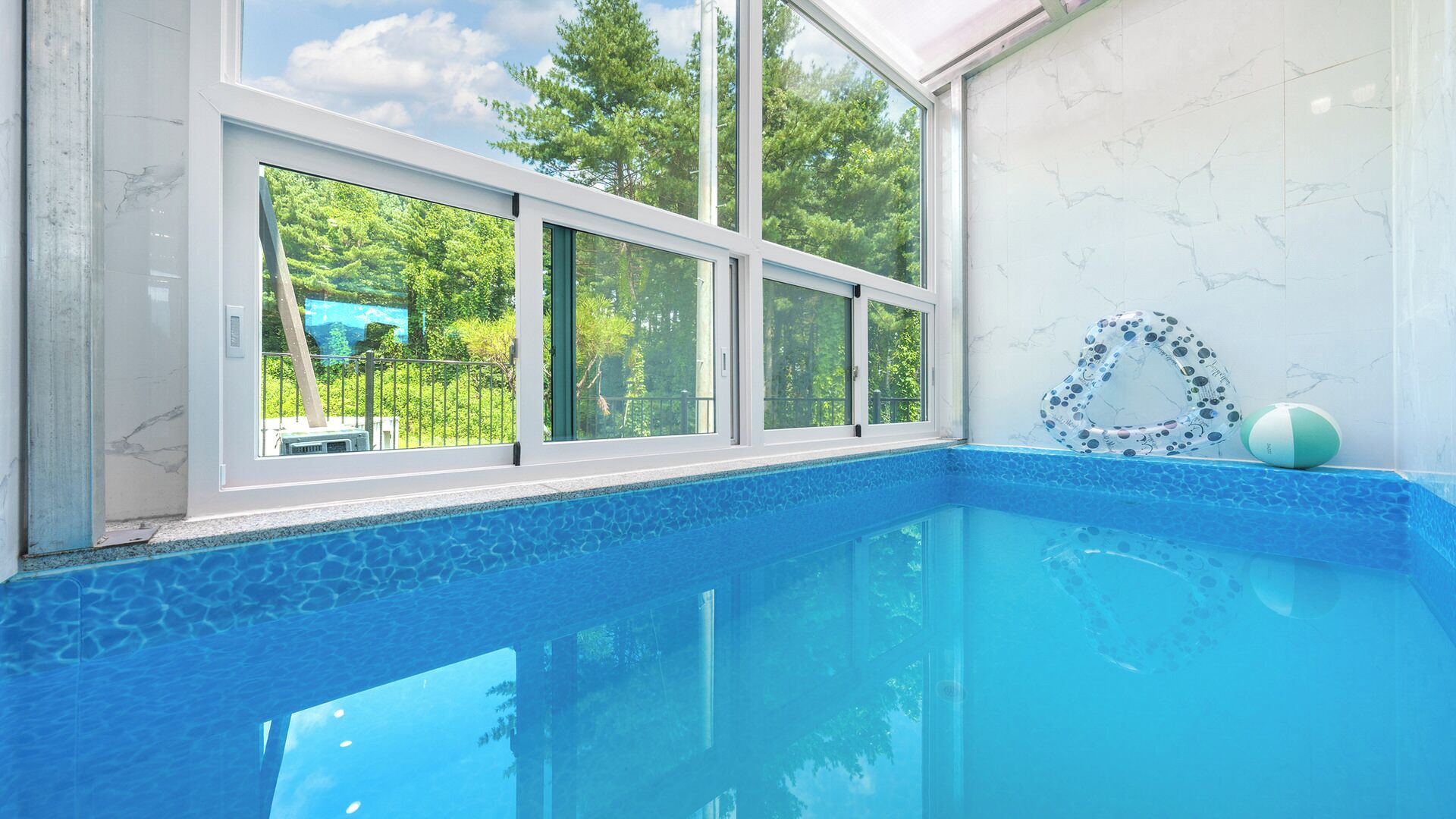 A swimming pool with a clear view of the outdoors through large windows.