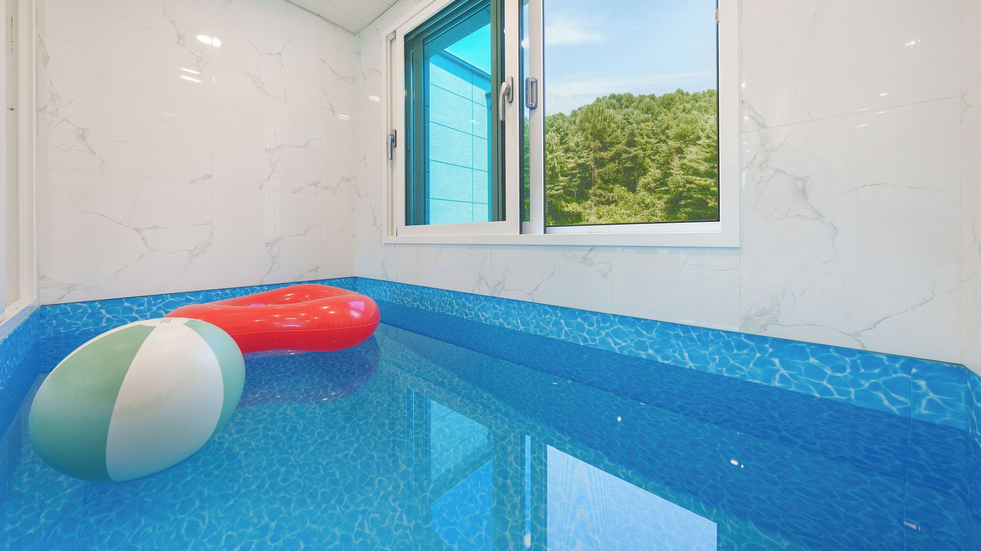 An indoor swimming pool with a clear view of the outdoors through a window.