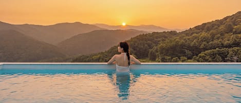 A person in a swimming pool with a sunset view over a mountainous landscape.