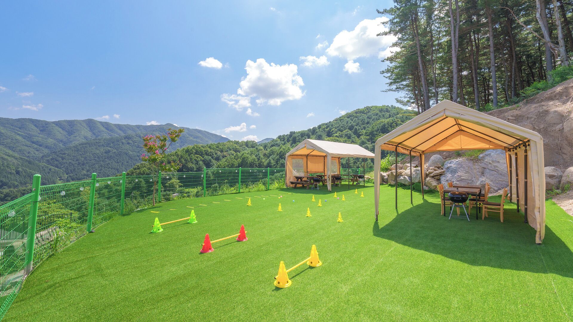 A campsite with two tents, a picnic table, and a grassy area with exercise cones.
