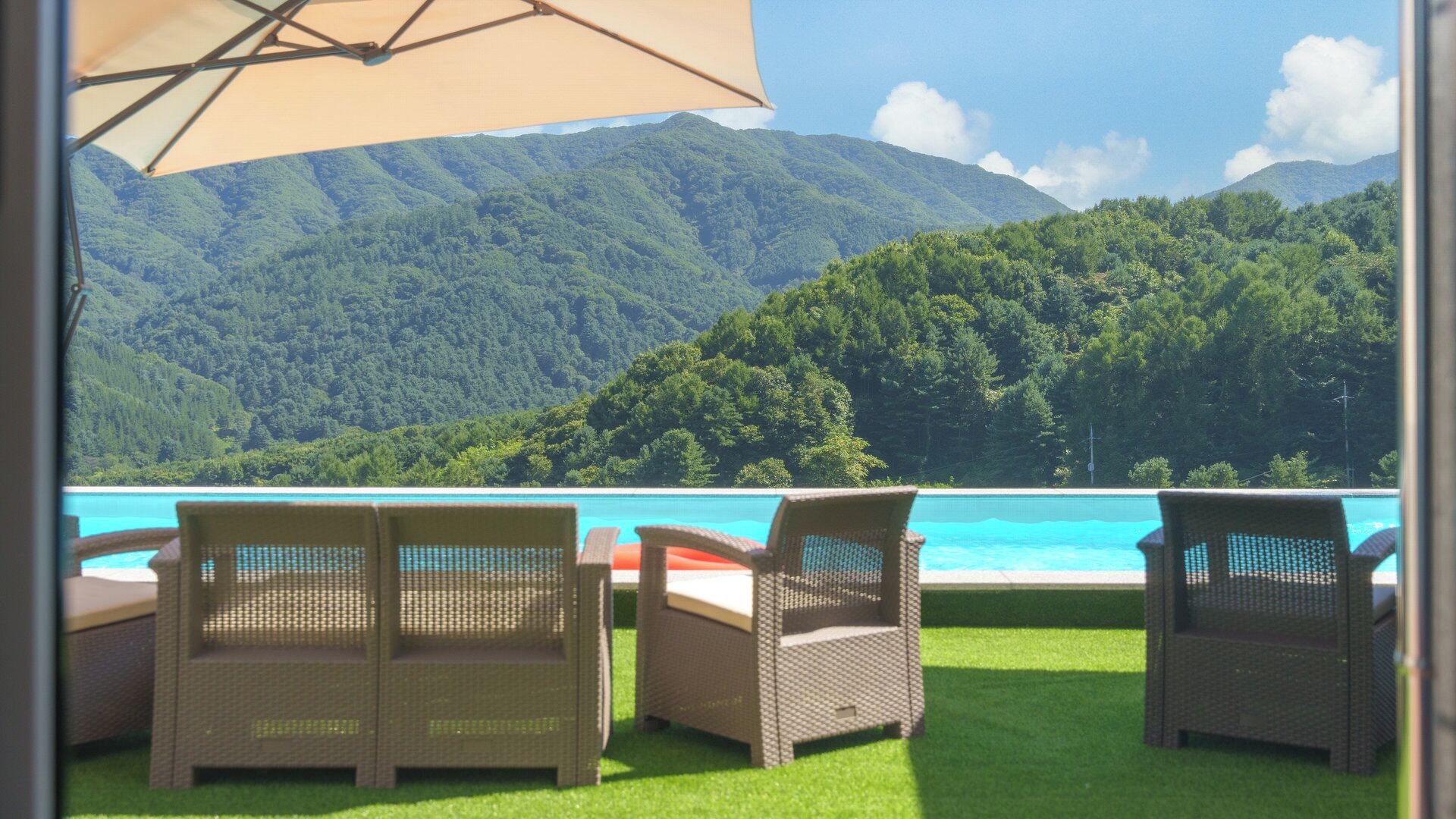 Una terraza con sillones de mimbre y una piscina, con vistas a un paisaje montañoso.