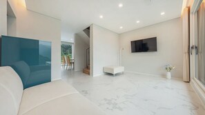 A modern living room with a white sofa, a flat-screen TV mounted on the wall, and a marble floor.