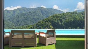 A poolside area with two wicker chairs and a view of a mountain and a body of water.