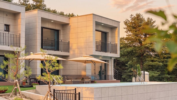 A modern multi-story building with balconies, outdoor seating, and a swimming pool.