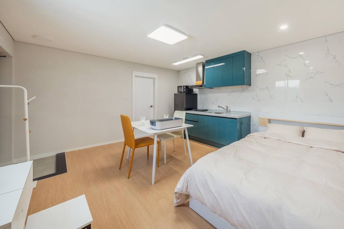 Une chambre compacte comprenant un lit, un petit bureau et une kitchenette.