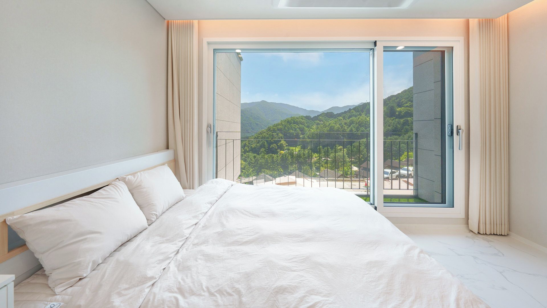 A bedroom with a bed, a nightstand, and a large sliding glass door leading to a balcony with a mountain view.