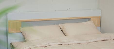 Un lit avec une tête de lit en bois et deux oreillers, placé contre un mur dont le motif ressemble à du marbre.
