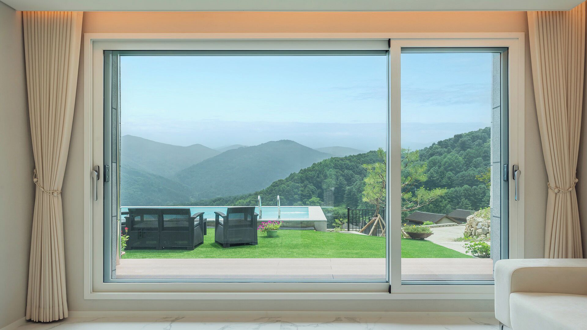 A room with a large sliding glass door leading to a balcony with a pool, chairs, and a view of mountains.