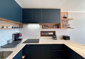 A modern kitchen with dark cabinets, a coffee machine, a kettle, and a toaster.