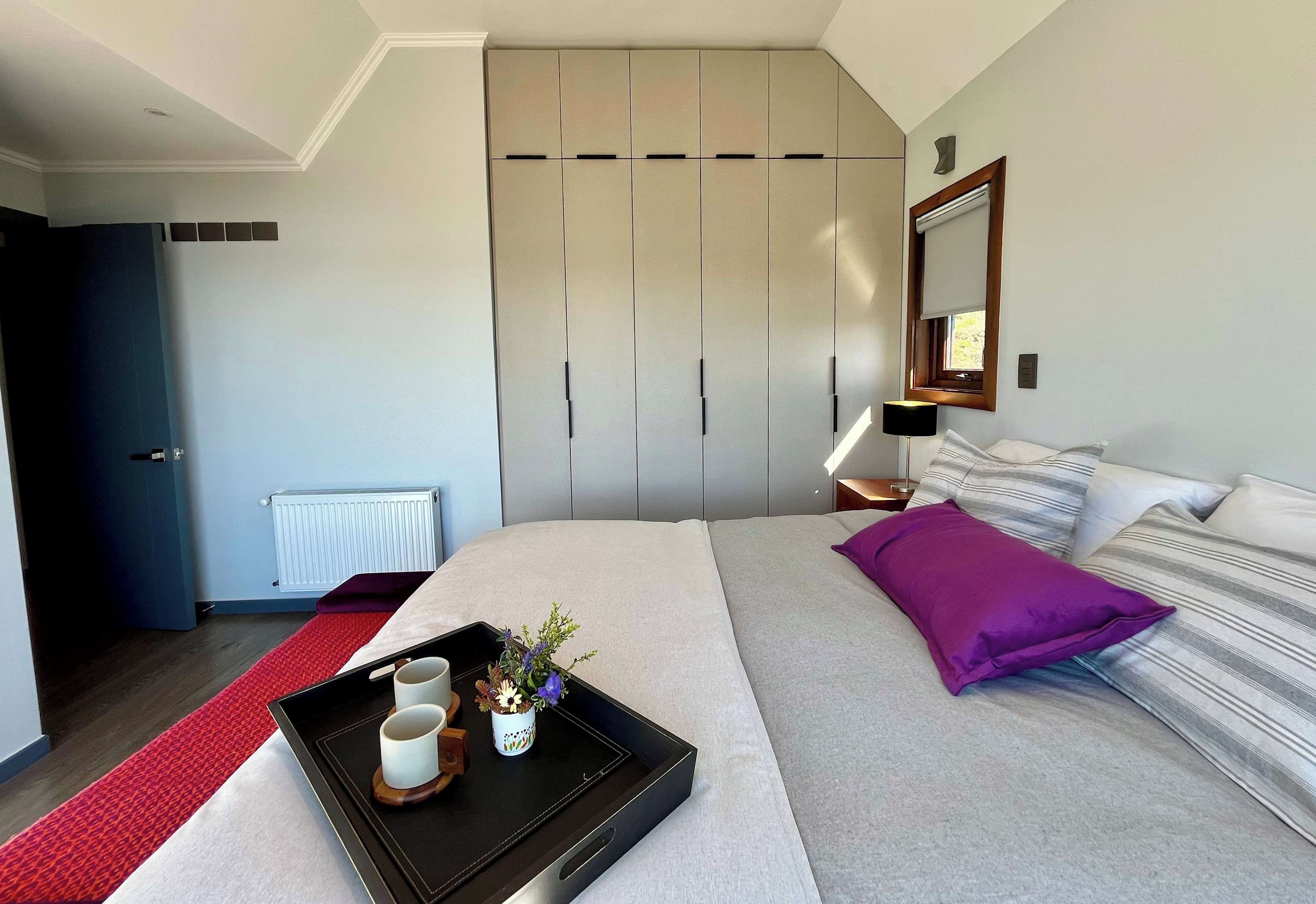 A modern bedroom with a bed, a bedside table, a nightstand, a dresser, and a window with a view.